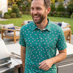 Man wearing a green soccer patterned polo shirt standing outdoors in a garden setting.