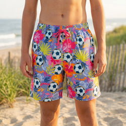 Person wearing colorful swim shorts with soccer ball pattern on a beach.