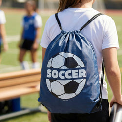 Person wearing a blue drawstring bag with a soccer ball design on a sports field.