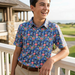 Young boy wearing a colorful soccer patterned polo shirt standing on a balcony with a scenic background.