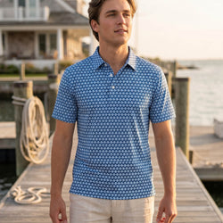 Teen wearing a blue soccer patterned polo shirt standing on a dock by a body of water.