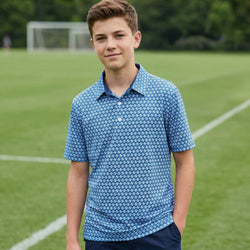Young boy wearing a blue soccer patterned polo shirt on a grassy field.