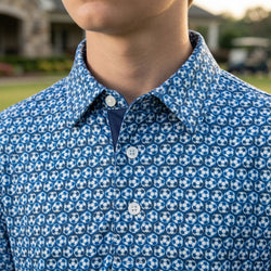 Person wearing a blue polo shirt with soccer ball pattern outdoors