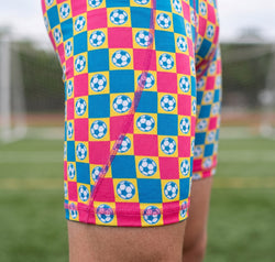 Colorful checkered shorts with soccer ball pattern on a sports field.