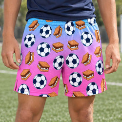Teen waeing purple to pink gradient colored shorts with soccer ball and smores pattern outdoors on a soccer field.