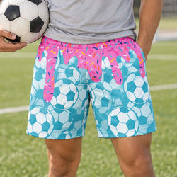Teen wearing blue soccer themed shorts with ice cream drip holding a soccer ball outdoors on a soccer field.