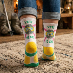 Person wearing socks with a Yeti design and text 'Yeti To Ski' in a home setting.