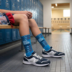 Person wearing blue swim socks with text sitting on a locker bench in a school hallway.