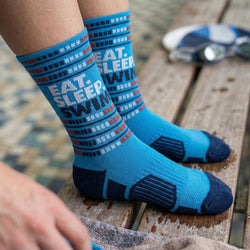 Blue socks with 'Eat. Sleep. Swim.' pattern on a wooden surface