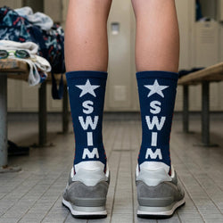 Person wearing blue socks with 'SWIM' and star designs in a locker room.