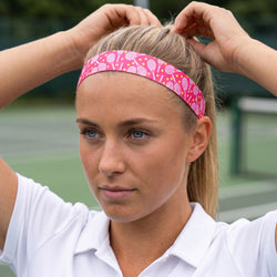 Woman adjusting a pink headband with a pattern on a tennis court