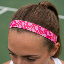 Person wearing a pink headband with tennis racket pattern on a tennis court