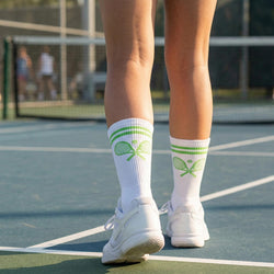 Person wearing white socks with green tennis racket design on a tennis court