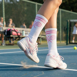 Person on a tennis court wearing white sneakers and socks with pink tennis racket designs.