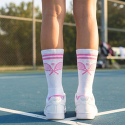 Person wearing white socks with pink accents and tennis shoes on a tennis court.