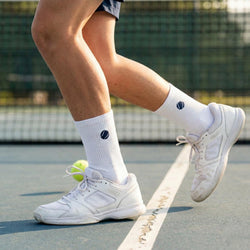 Person wearing white sneakers and tennis socks on a tennis court