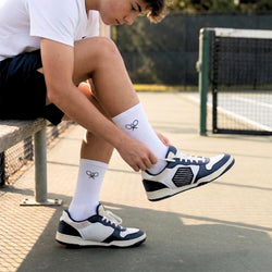 Person with wite tennis socks tying their shoe on a tennis court