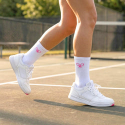 Person wearing white sneakers and socks with pink accents on a tennis court.