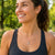 A smiling woman outdoors wearing a delicate silver necklace with a small running figure pendant, paired with a black athletic tank top.