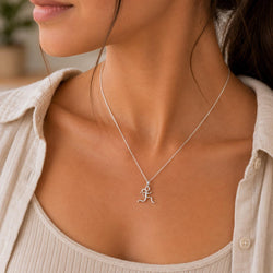 A close-up of a woman wearing a delicate silver necklace with a small running figure pendant, styled with a light beige linen shirt.