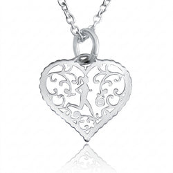 A silver filigree heart pendant necklace featuring a cutout design with a central figure and scrollwork, suspended from a matching silver chain on a white background with a soft reflection below.