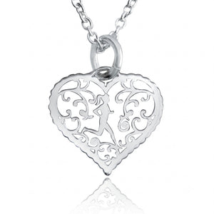 A silver filigree heart pendant necklace featuring a cutout design with a central figure and scrollwork, suspended from a matching silver chain on a white background with a soft reflection below.