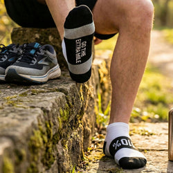 Person wearing black and white socks with motivational text, sitting on a stone path outdoors.