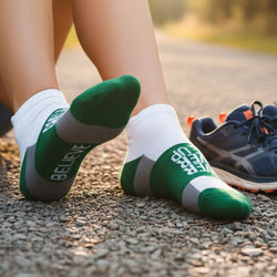 Person wearing green and white socks with motivational text, sitting on a road.