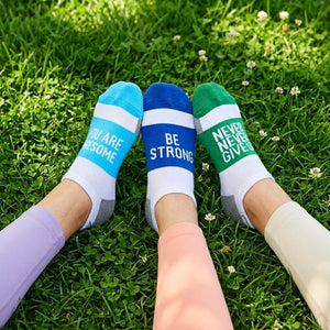 Three pairs of socks with motivational phrases on a grassy background