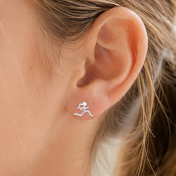A close-up of a person's ear wearing a small silver stud earring shaped like a running figure, with light brown hair visible.