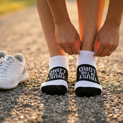 Person wearing black and white socks with motivational faith text, standing on a gravel path.