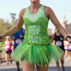 A woman running during a race wearing a bright green athletic tank top with the text 'POWERED BY PIXIE DUST' and a matching green tulle tutu skirt.