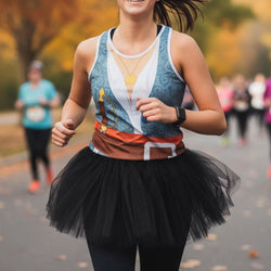 A woman running outdoors wearing a pirate inspired tanktop with a blue, white, and orange graphic print, a black tutu skirt, and black leggings. The background shows a blurred park path with other runners.