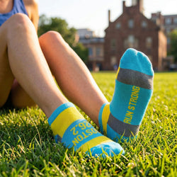 Person wearing blue and yellow boston 26.2 socks with 'Run Strong' text, sitting on grass.