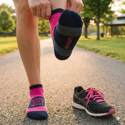 Person wearing pink and black socks with motivational text, standing on a path in a park.