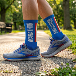 Person wearing blue socks with 'Marathon' text and gray running shoes on a path outdoors.