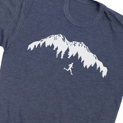 A close-up of a heather navy blue t-shirt featuring a white graphic print of a mountain range with pine trees and a small running figure.