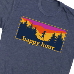 A close-up of a heather navy blue t-shirt featuring a rectangular graphic on the chest. The graphic shows a silhouette of a runner against a sunset gradient of purple, orange, and yellow, with pine trees and the text 'happy hour' in yellow.