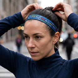 Woman adjusting a headband with 'NYC 26.2' text on a city street.