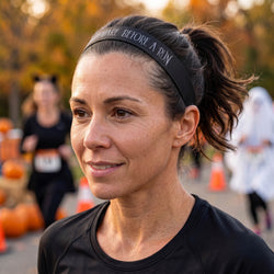Woman wearing a black headband with halloween text, standing in a race setting with blurred background