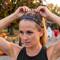 Woman adjusting a headband with 'Nightmare Before a Run' text in an outdoor setting.