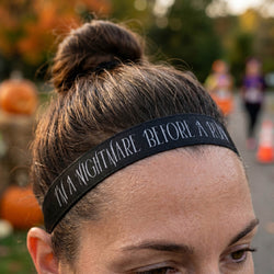 Person wearing a headband with halloween text, surrounded by pumpkins and blurred people in the background