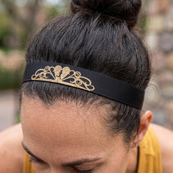 Person wearing a black headband with gold decorative elements on a blurred outdoor background