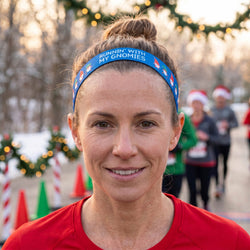 Woman wearing a blue headband with text, smiling at a festive running event.