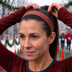 Woman adjusting a headband with a festive pattern, surrounded by Christmas decorations and people in the background.
