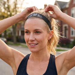Woman adjusting a headband with a blurred outdoor background