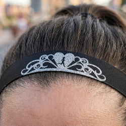 Black headband with decorative silver design on a person's head against a blurred background