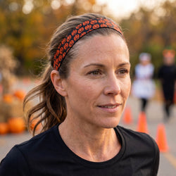 Woman wearing a black shirt and black headband with pumpkin design, standing outdoors with blurred background