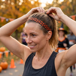 Woman adjusting a headband with pumpkin design outdoors at a fall event.