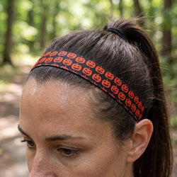 Person wearing a Halloween-themed headband with jack-o'-lanterns, blurred background of people in orange shirts.